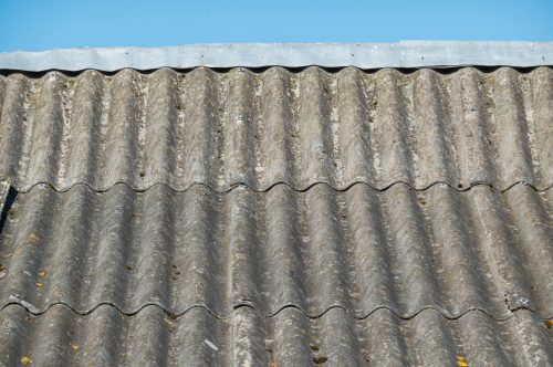 A fragment of an old roof made of gray corrugated asbestos-cement sheets. The surface is covered with moss. There is a metal ridge on the roof. Background. Texture.